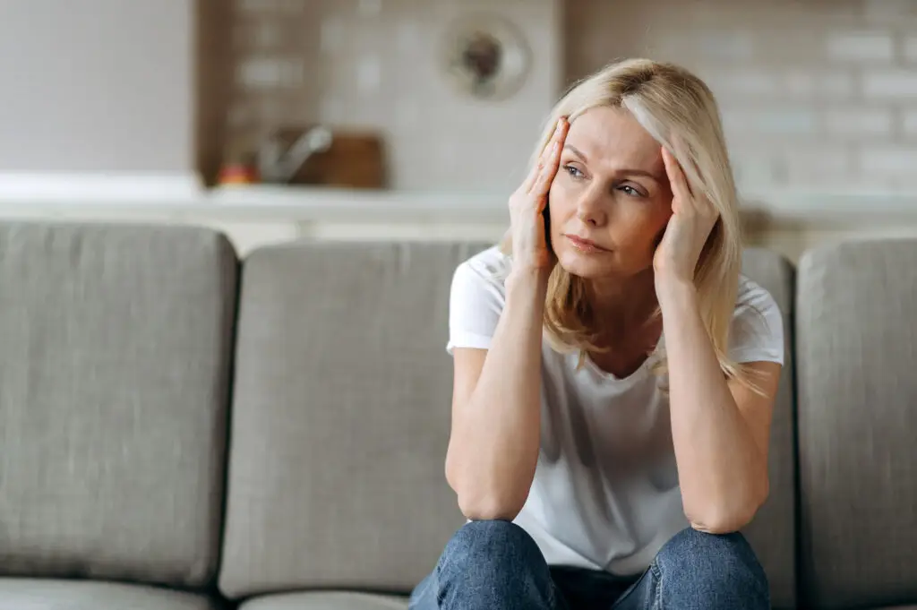 senior woman sitting on a couch looking fatigued.